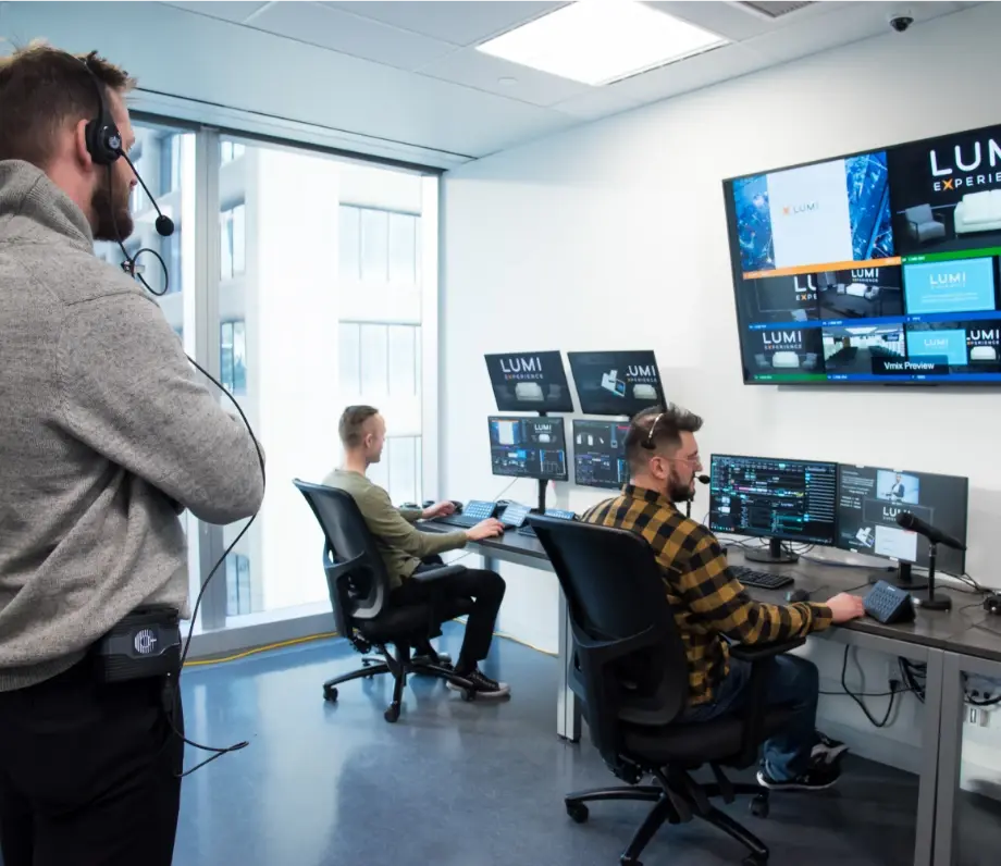 2 men working on multiple screens while another man with a headset looks on