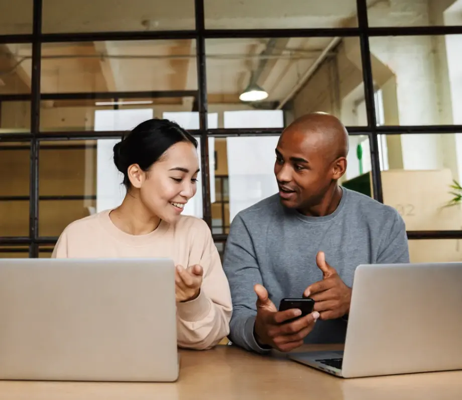 Man and woman on laptops looking at a phone one is holding