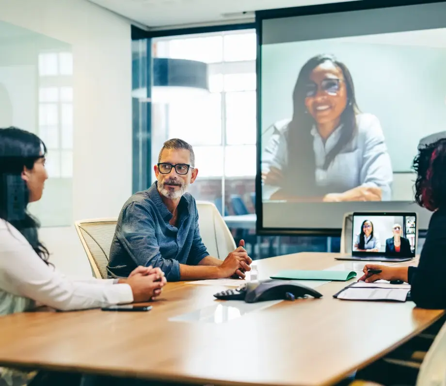 Three people in meeting room with another person on a projector